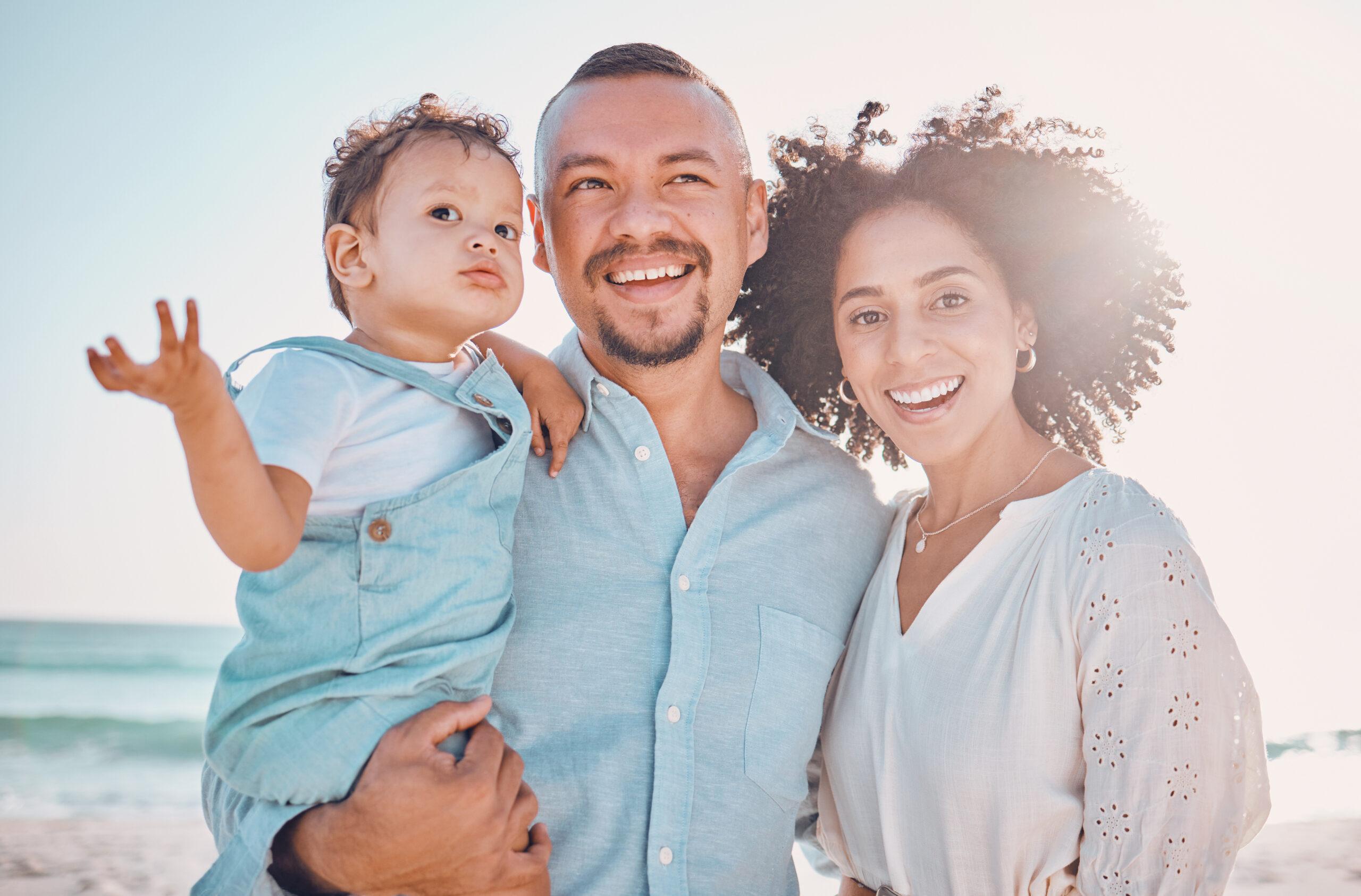 A young family smiling on a beach.