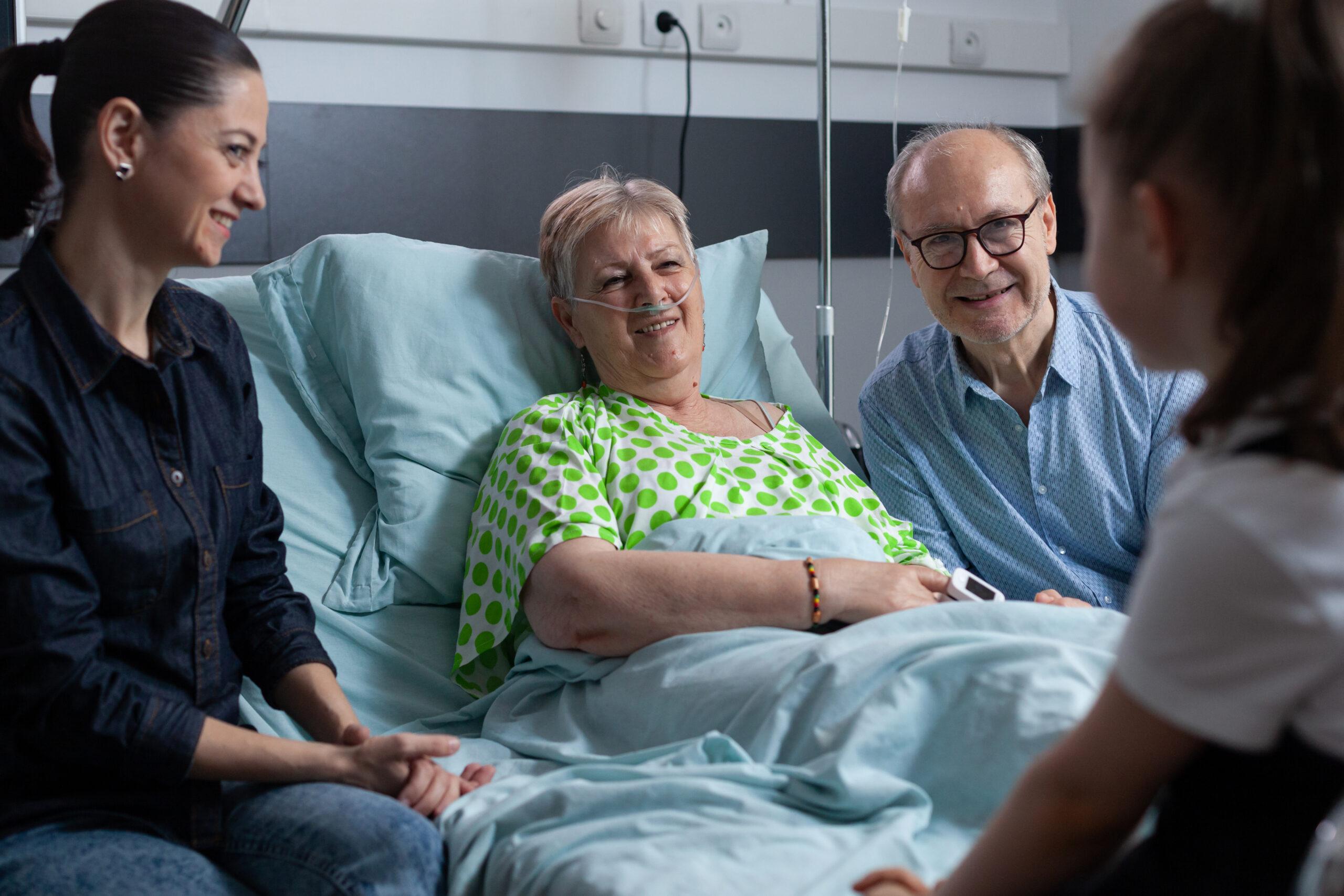 Girl talking with grandparents at hospital recovery room. Young woman with daughter seeing elderly couple in geriatric clinic medical observation room.