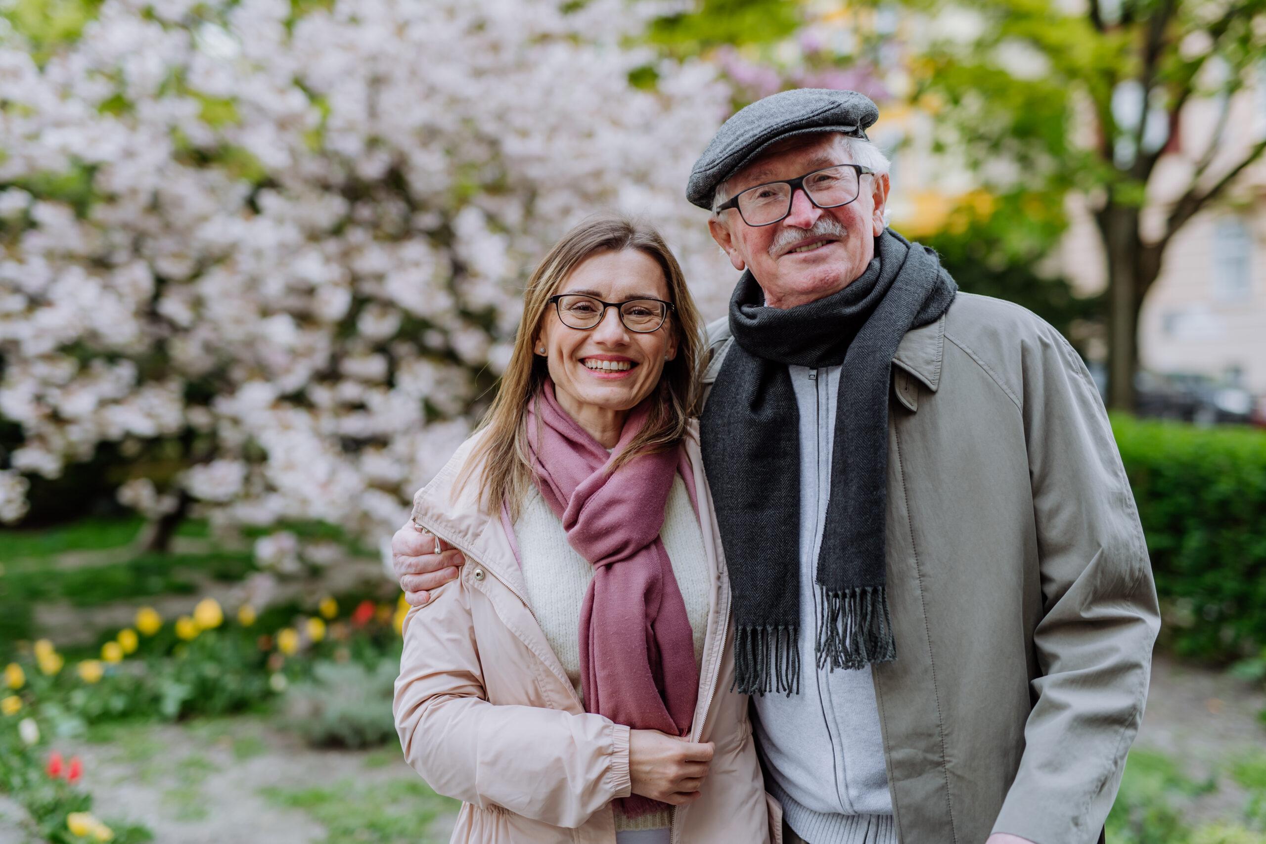 Daughter hugging her senior father outdoors in park on spring day.