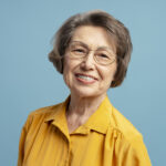 Cheerful elderly woman with glasses and yellow shirt smiles on blue background