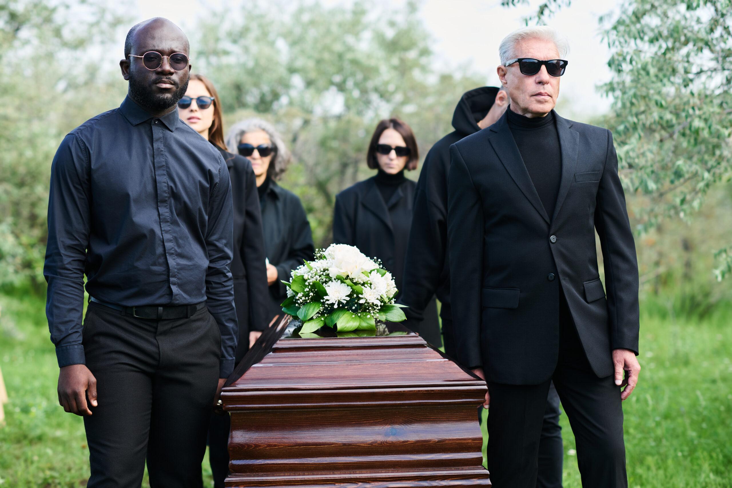 Group of grieving people in mourning attire carrying wooden coffin