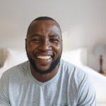 Portrait of happy african american man looking at camera and smiling in bedroom