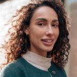 Portrait of young woman in green coat with curly hair in the city close up