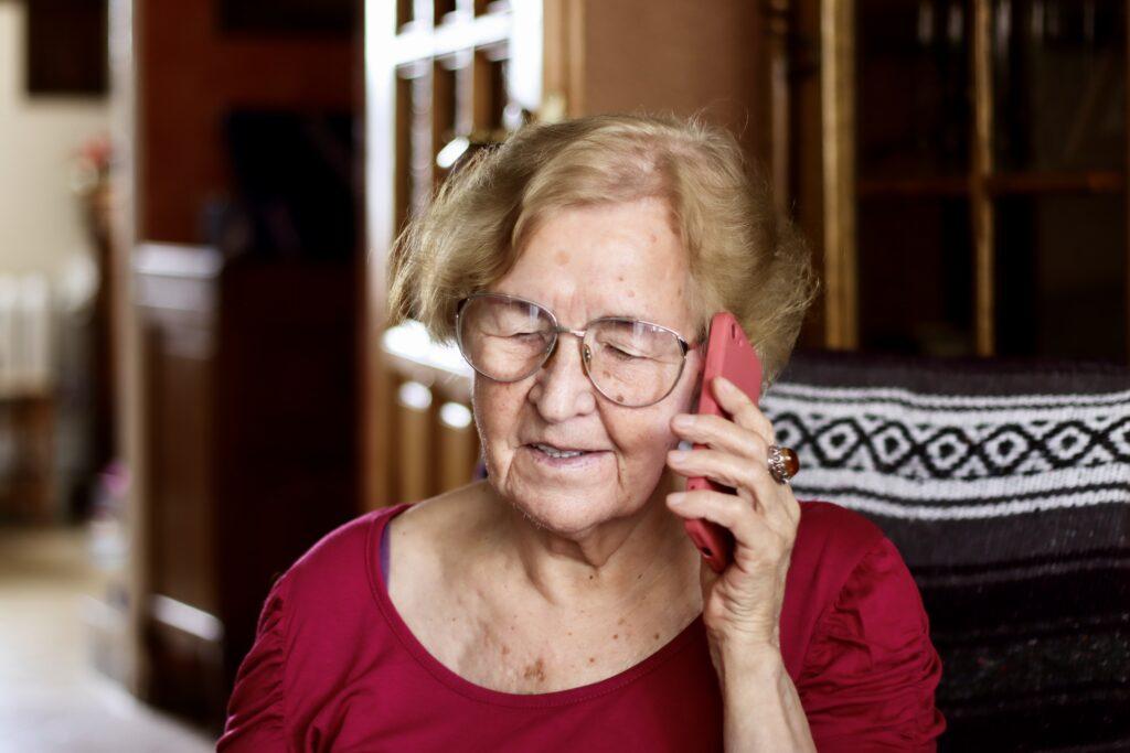 A grandmother wearing a red shirt talking to someone on a phone.