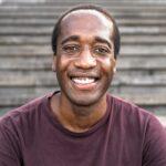 Happy African man smiling into the camera while sitting on urban stairs