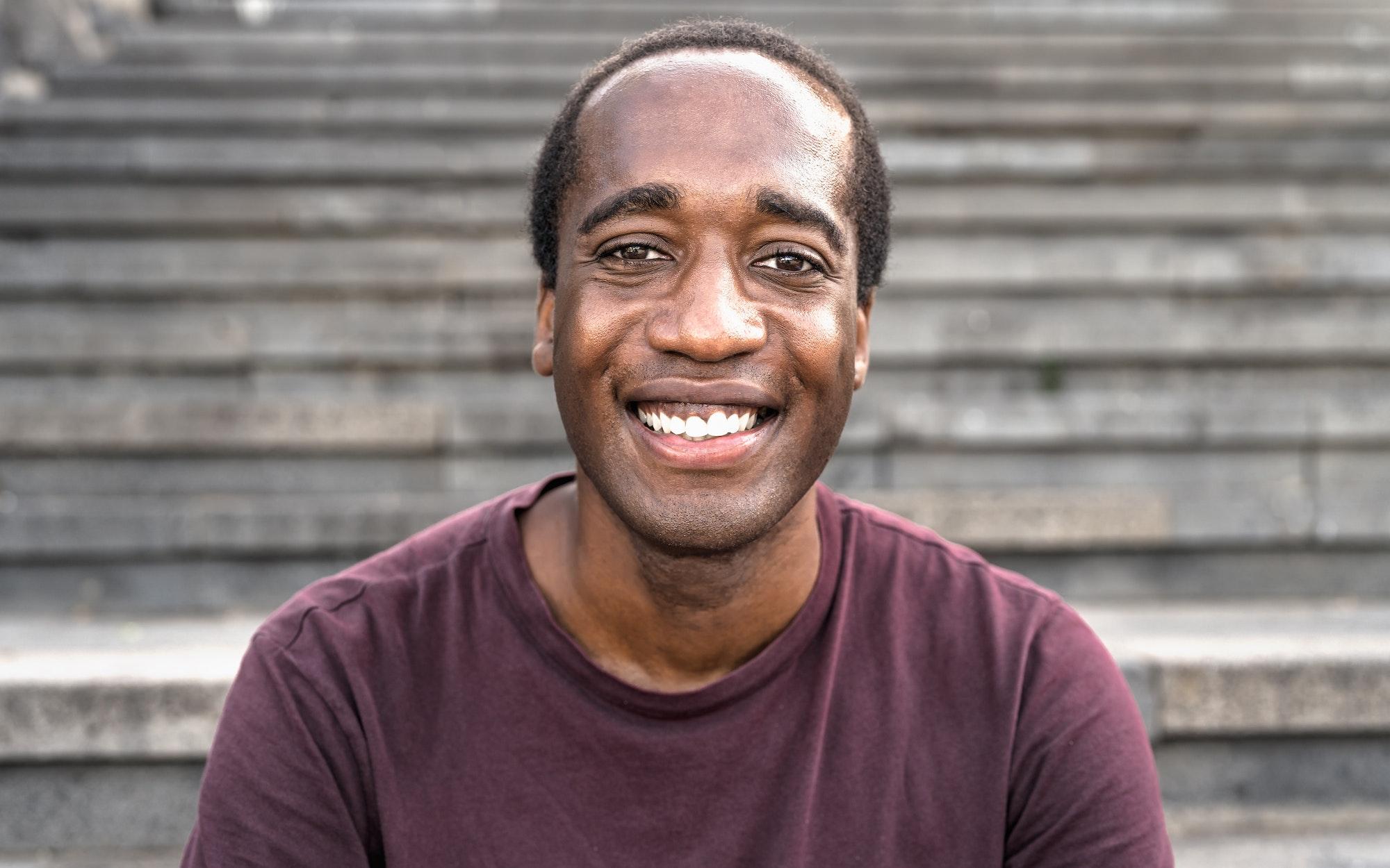 Happy African man smiling into the camera while sitting on urban stairs