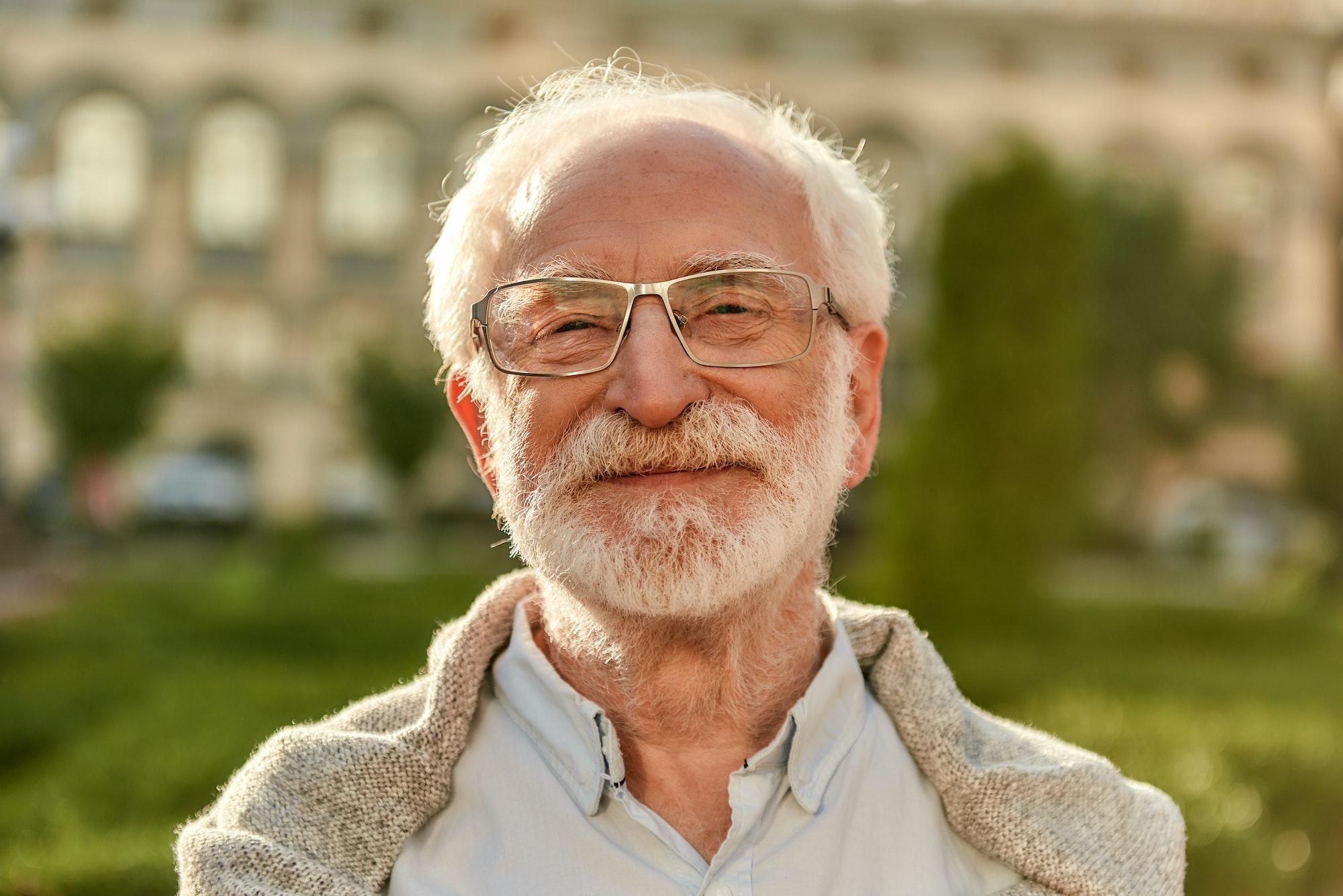 Positive attitude. Portrait of handsome bearded senior man in glasses looking at camera and smiling
