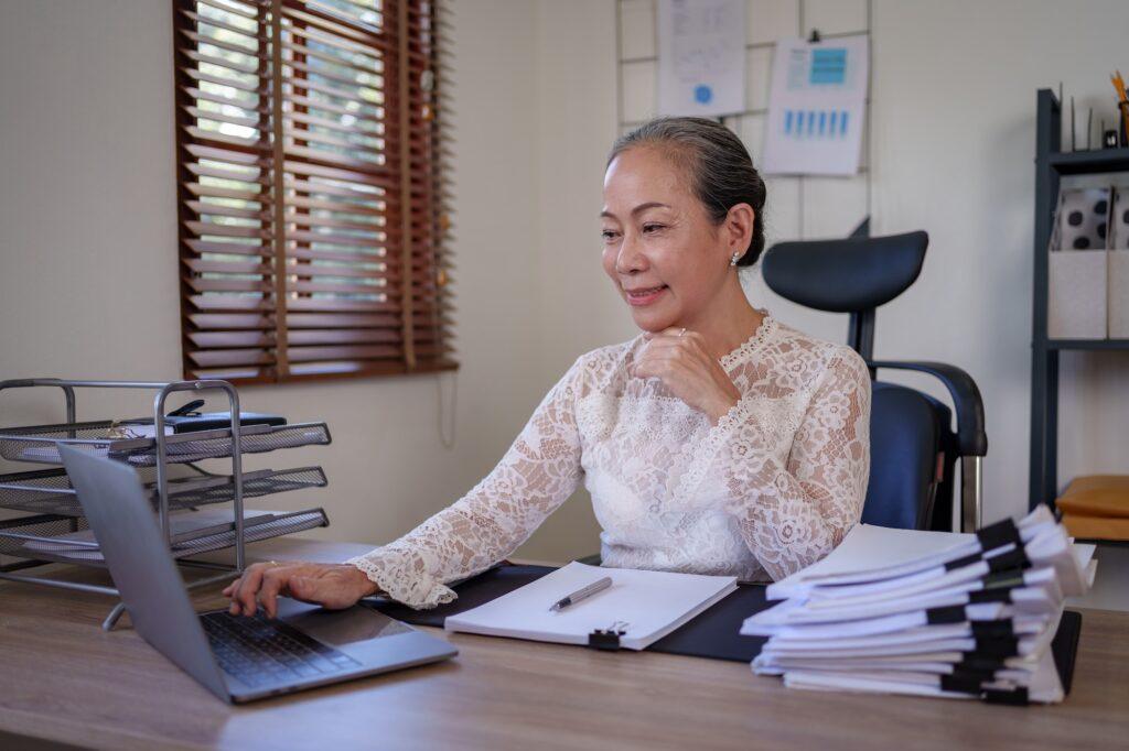 Senior asian business woman reviewing limited pay life insurance policies at a desk.
