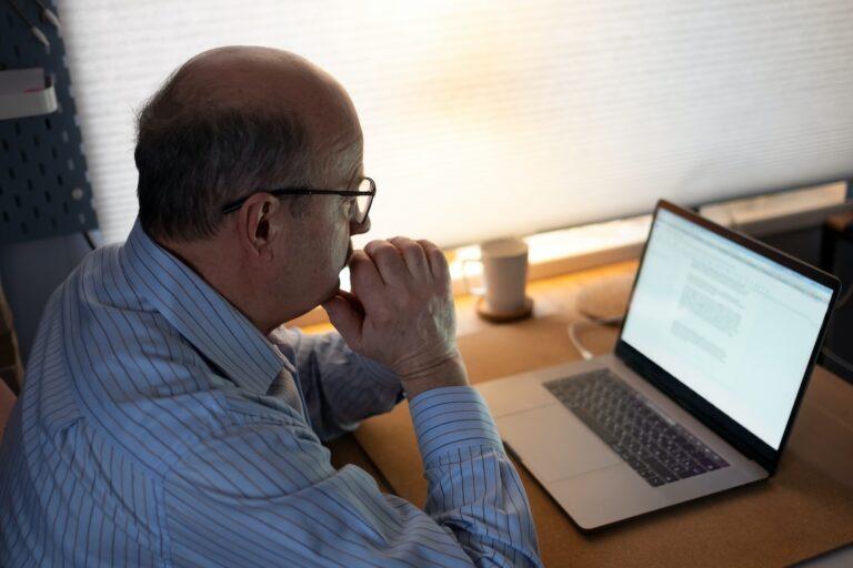 Senior man working with laptop computer at home and thinking on document.
