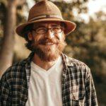 Smiling bearded man in glasses and hat in nature