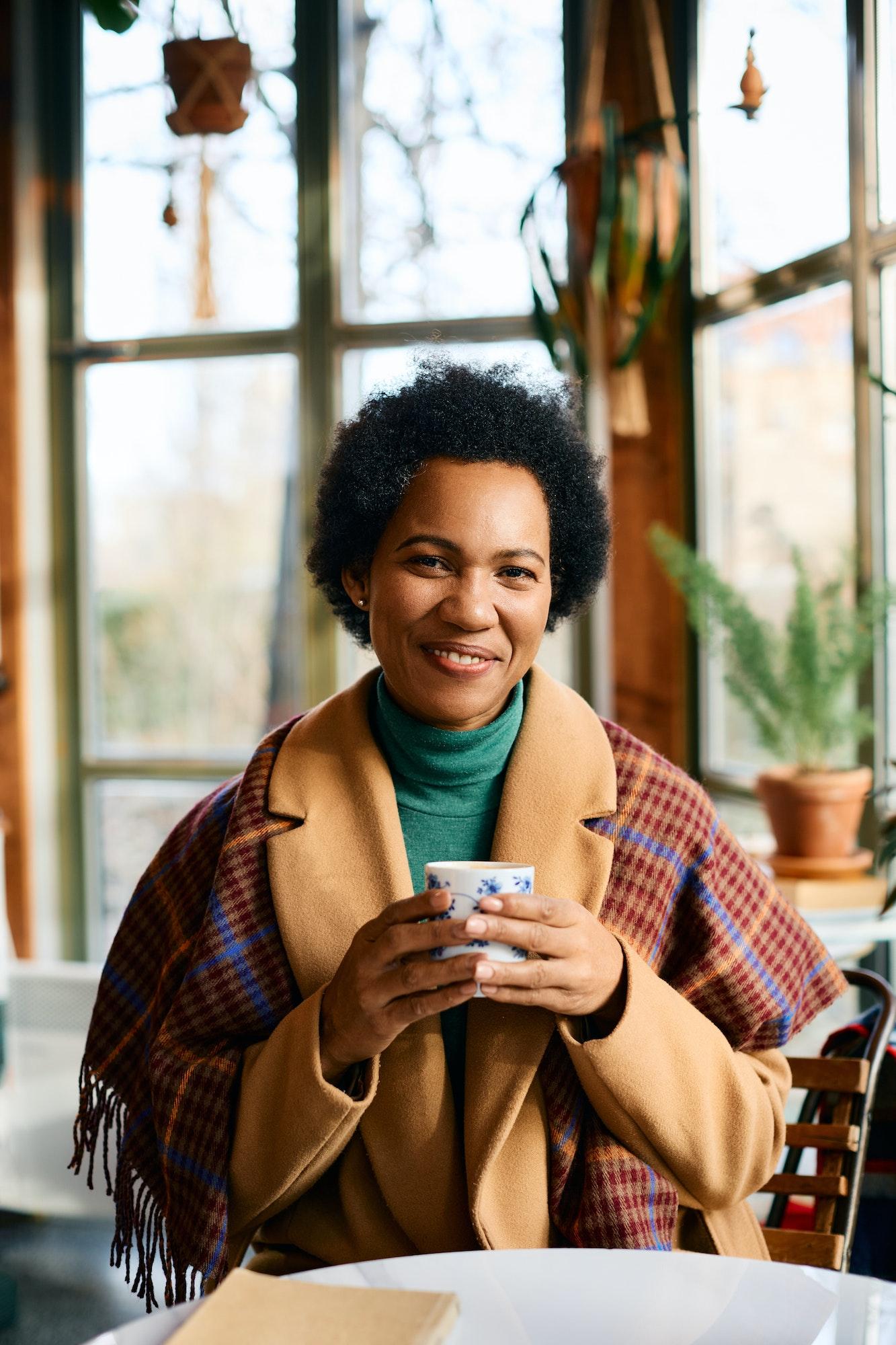 Happy African American woman enjoying in cup of tea in cafe during winter season.