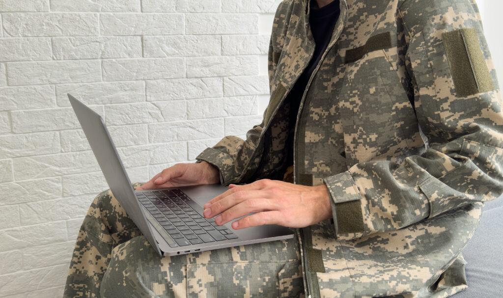 A soldier looking at a laptop on their lap.