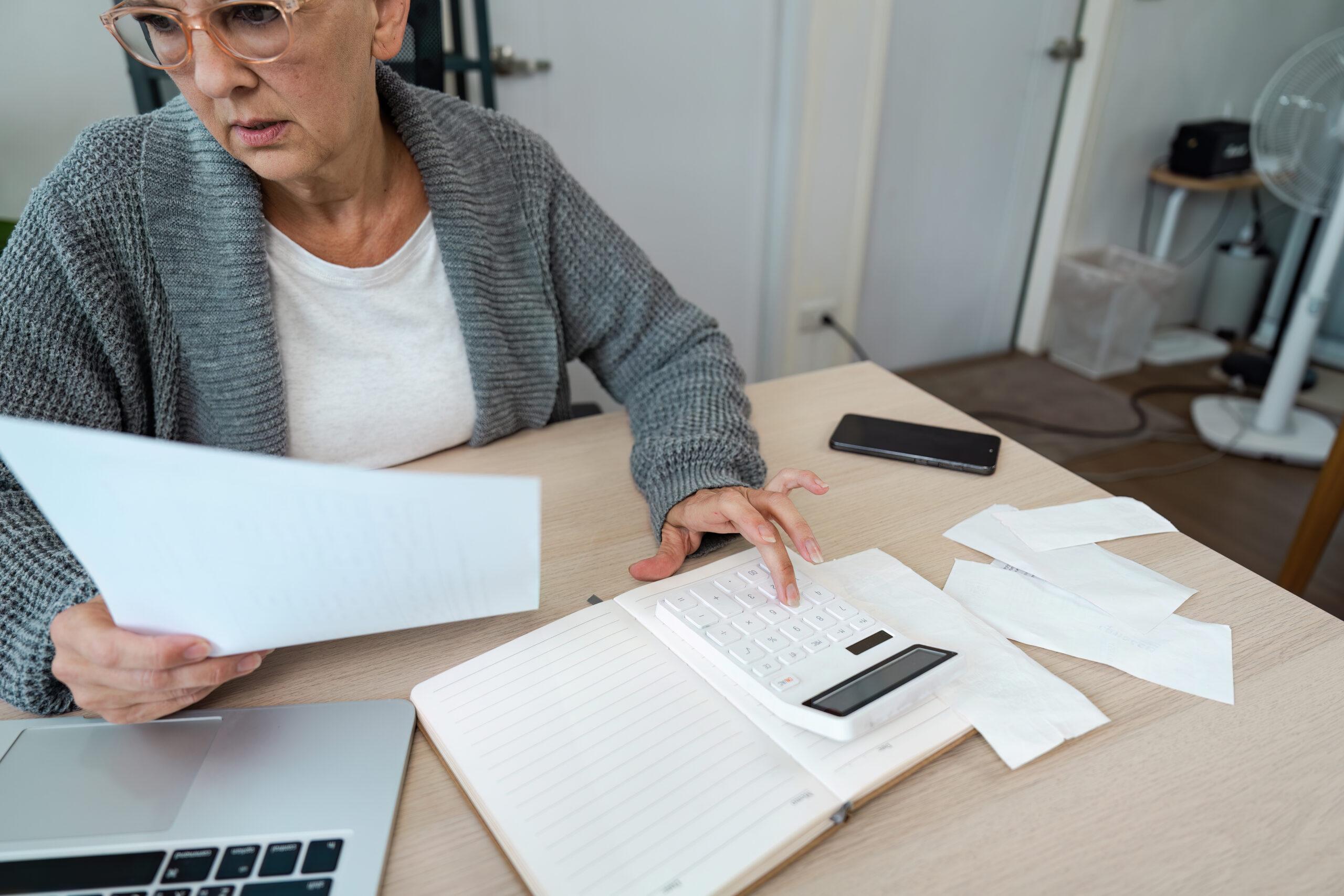 A woman seated at a desk reviewing financial paperwork and using a calculator.