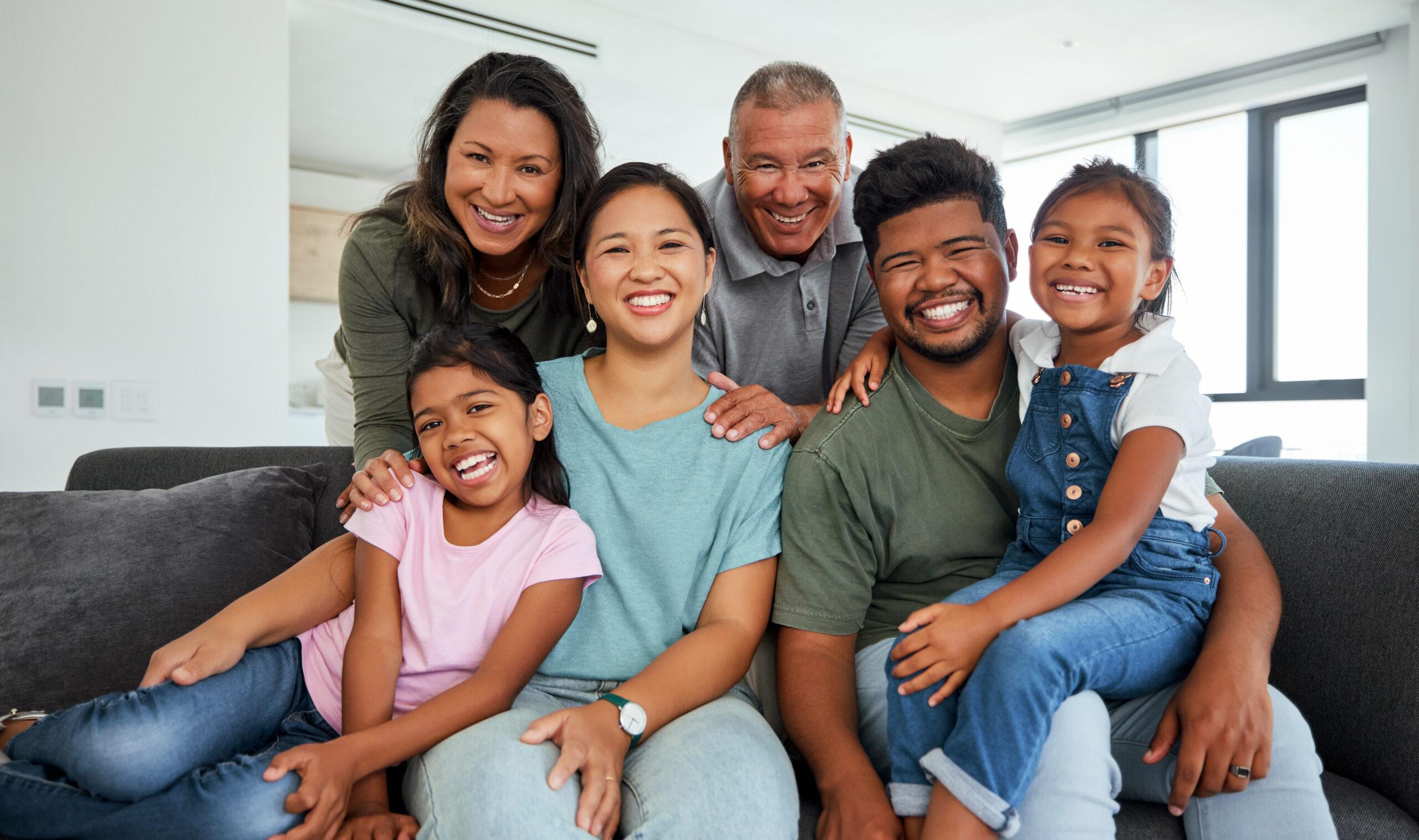 A family with children, parents, and grandparents sits smiling on a sofa.