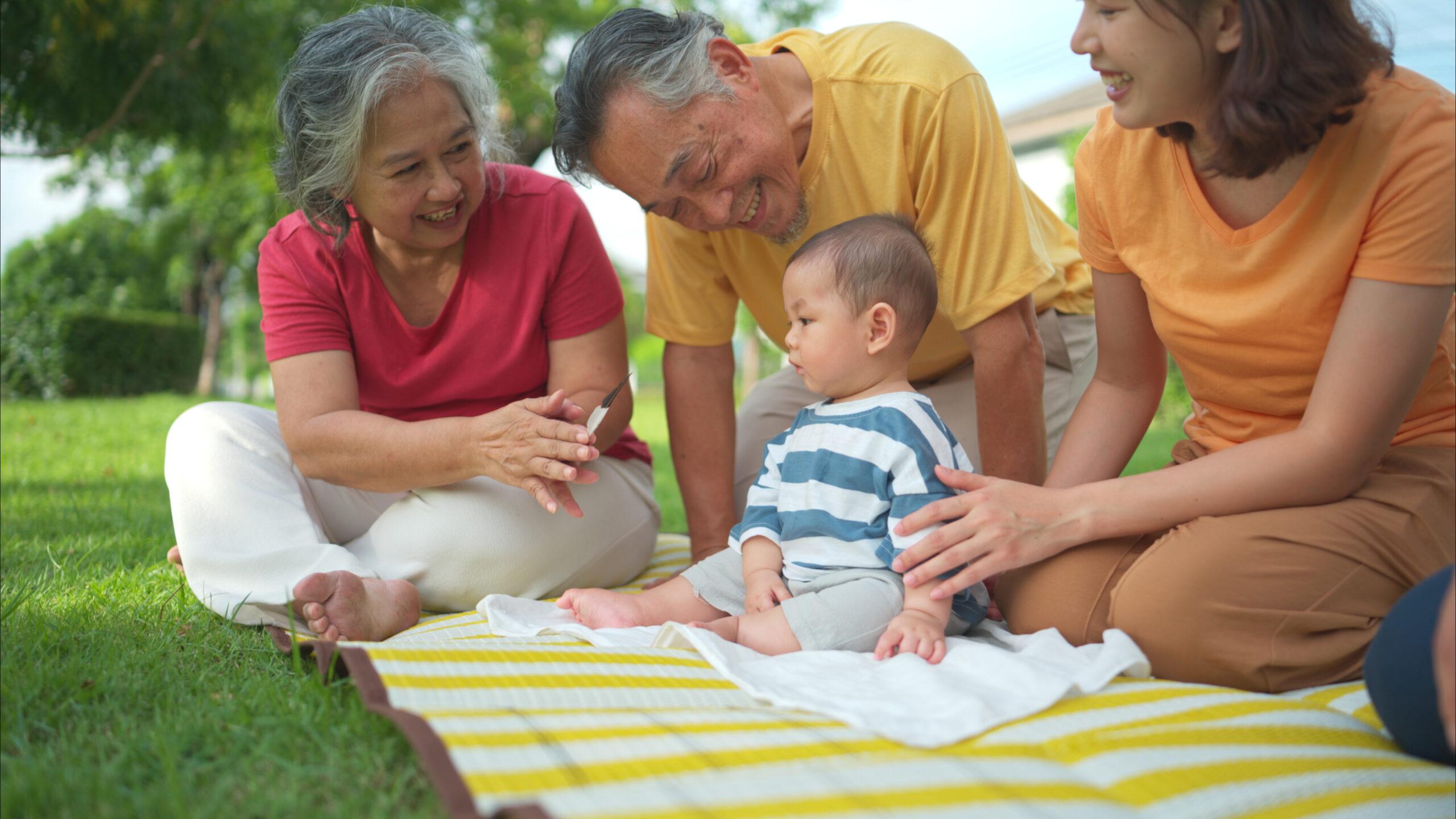 Grandparents and parents with little child are having fun and resting in a park