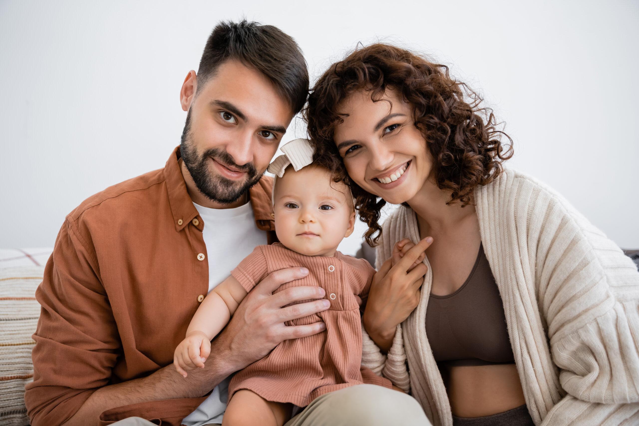 portrait of cheerful father holding happy infant daughter near smiling wife