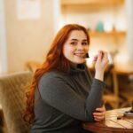 A young woman looking into the camera while eating a piece of cake.