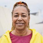 A senior woman wearing a yellow jacket and looking into the camera.