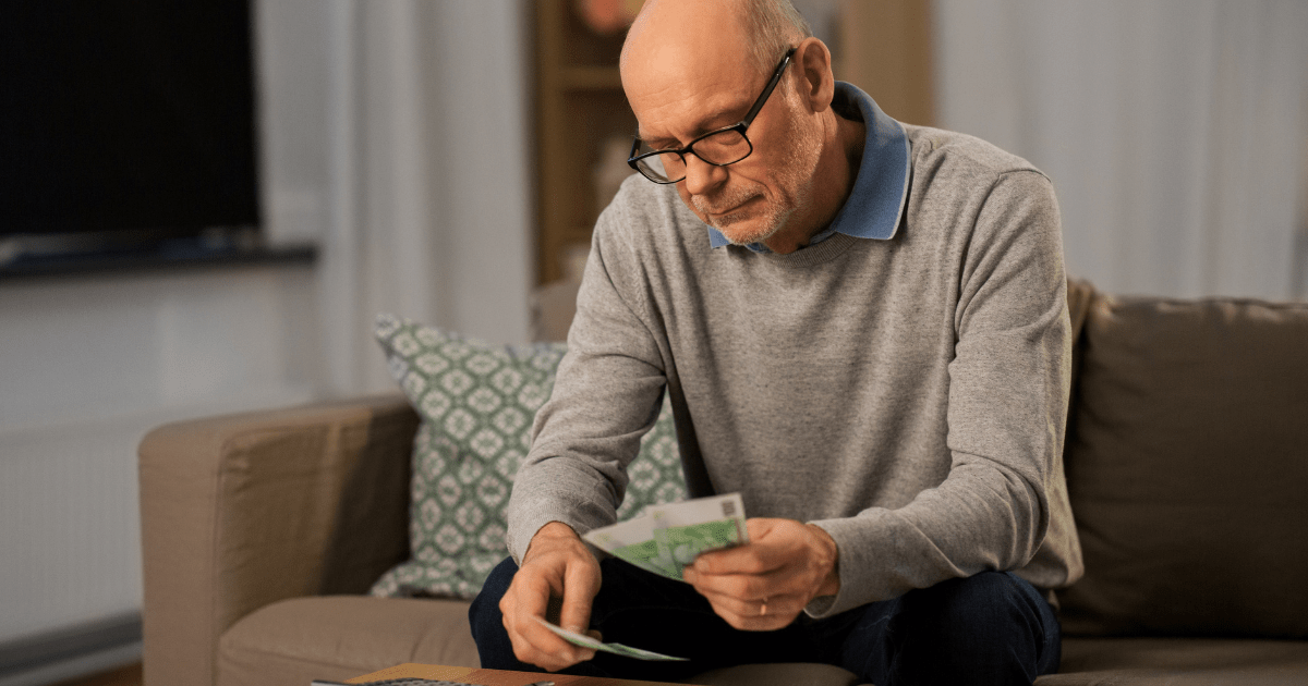 Older man on couch viewing money that he has saved