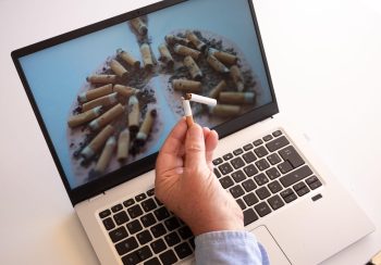 Adult hand holding a broken cigarette over laptop keyboard, ready stop smoking. World tuberculosis day, world no tobacco day, corona virus covid-19, biological air pollution; organ donation concept