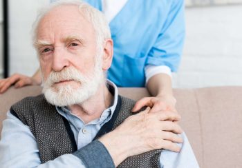 Cropped view of nurse standing behind senior man, putting hand on his shoulder