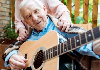 cropped view of senior woman near happy retired husband playing acoustic guitar