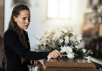 Funeral, sad and woman with flower on coffin after loss of a loved one, family or friend. Grief, de.