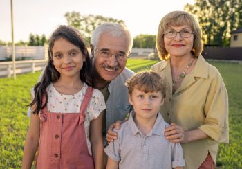 Cheerful grandparents in eyeglasses standing by their two cute grandchildren