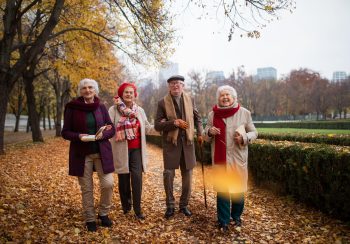 A group of happy senior friends with books on walk outdoors in park in autumn, talking and laughing