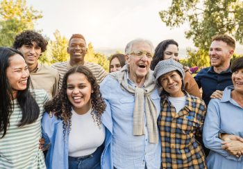 Group of multigenerational people smiling in front of camera - Multiracial friends of different ages having fun together - Main focus on caucasian senior face