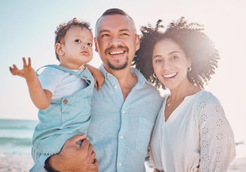 A young family smiling on a beach.