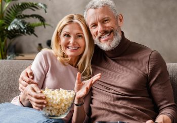 Happy middle aged couple, wife and husband watching tv and eating popcorn