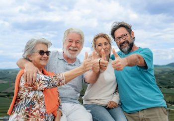 Happy multi generation family having fun together on outdoor countryside excursion, gesturing thumbs up to the camera. Parents, son and daughter-in-law enjoying free time and recreational activities