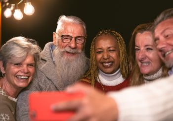 Happy multiracial senior friends having fun in holidays taking selfie with mobile smartphone on house patio - Elderly lifestyle people concept