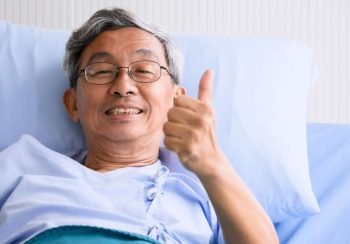 Male patient smiling and lying down on sickbed in hospital room.