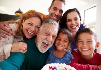 Multi-Generation Hispanic Family Taking Selfie To Celebrate Granddaughters Birthday At Home