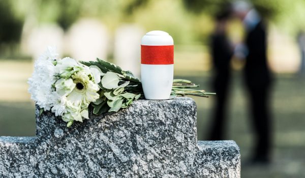 A cremation urn on top of a gravestone beside some flowers.