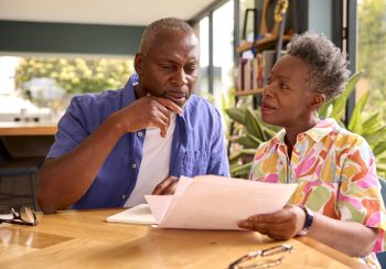 Senior Couple Sitting Around Table At Home Reviewing Finances