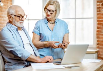 Beautiful senior couple in blue shirts working together with laptop on the kitchen at home