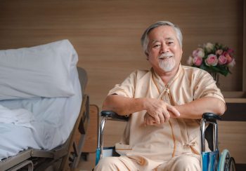 Senior male patient sitting on wheelchair in hospital smiling and talking and showing something outside the window to handsome doctor in labcoat in room