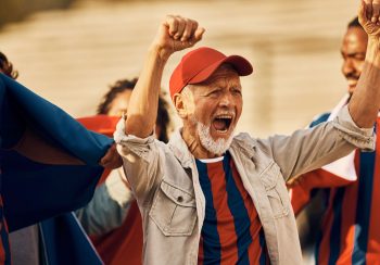Excited senior soccer fan cheering for his team during sports championship.