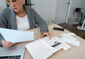 A woman seated at a desk reviewing financial paperwork and using a calculator.